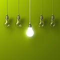 One hanging light bulb glowing different and standing out from unlit incandescent bulbs with reflection on green background Royalty Free Stock Photo