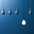 One hanging light bulb glowing and standing out from unlit incandescent bulbs on dark blue background Royalty Free Stock Photo