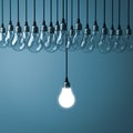 One hanging light bulb glowing with unlit incandescent bulbs on dark cyan background Royalty Free Stock Photo