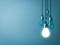 One hanging light bulb glowing with unlit incandescent bulbs on dark green pastel color background Royalty Free Stock Photo