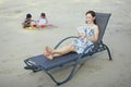 Woman sitting on beach chair reading book, boy and girl playing with sand in the background. Conceptual image Royalty Free Stock Photo