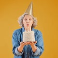 One happy mature caucasian woman blowing out candles on a cake she is holding while wearing a birthday hat against a Royalty Free Stock Photo