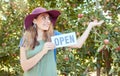 One happy woman holding open sign to advertise apple picking season on sustainable orchard farm outside on a sunny day