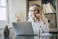 One happy young adult freelance at work in home office. Professional woman with laptop using phone to call remote clients. Help Royalty Free Stock Photo