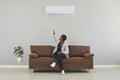 Black woman sitting on couch and switching her air conditioner with remote control Royalty Free Stock Photo