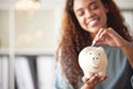 One happy young mixed race woman holding a piggybank and depositing a coin as savings. Hispanic woman budgeting her