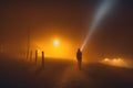 One human silhouette with flashlight in foggy countryside street at night in the orange light