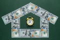 One hundred american dollars house and yellow alarm clock over green background. Mortgage concept.