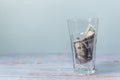 One hundred banknote rolled up in the glass on a wooden table and a blue background. Copy space, saving money concept