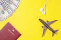 One hundred dollar bills, airplane, headphones, foreign passport on bright yellow paper background. Copy space.