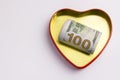 One hundred dollars in a gold heart shaped box with a red outline. Concept for the holiday St. Valentine`s Day, a gift Royalty Free Stock Photo