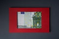 One hundred euro banknote in a red cardboard frame on a gray background