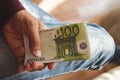 One hundred euro banknotes in tanned left hand of man in burgundy sweater against the background of leg in jeans Royalty Free Stock Photo