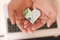 one hundred euro paper money in shape of heart in men& x27;s palms on background of laptop, selective focuse Royalty Free Stock Photo