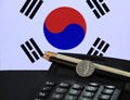 One hundred Korean won coin on obverse, KRW on black calculator with black and white pencil on black floor and Korean flag.