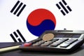 One hundred Korean won coin on reverse, KRW on black calculator with black and white pencil on black floor and Korean flag.