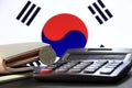 One hundred Korean won coin on reverse, KRW on black calculator with wallet on black floor and Korean flag background.
