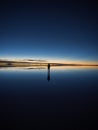 One isolated male tourist enjoying andes mountains sunrise mirror reflection on Salar de Uyuni salt flat lake in Bolivia