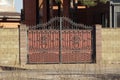 One large brown closed metal gate with a black wrought iron pattern and part of a brick wall Royalty Free Stock Photo