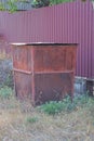 one large closed brown rusty iron trash can stands in dry grass on the ground Royalty Free Stock Photo