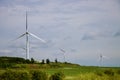 Wind turbines reflecting sun on a cloudy day in green rolling fields