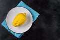 One lemon on a white plate on a blue napkin on a black background. Trendy ugly organic fruit.