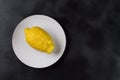 One lemon on a white plate on a dark natural colored background in Horizontal orientation. Trendy ugly organic fruit.