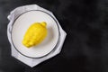 One lemon on a white plate on a light kitchen towel on a black background. Trendy ugly organic fruit.