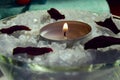 one lit candle that stands in a glass bowl with salt for a bath with rose petals. selective focus Royalty Free Stock Photo
