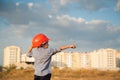 One little boy builder in orange helmet pointing finger towards building on sunset and blue cloudy sky with copy space Royalty Free Stock Photo