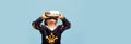 One little boy in costume of medieval pageboy, little prince wearing VR headset standing over blue background. Emotions