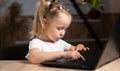 One little preschool girl in the evening sits at home at a table with a laptop with her fingers focused and is typing Royalty Free Stock Photo