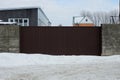 One long brown metal gate and a gray concrete fence wall on a winter street Royalty Free Stock Photo