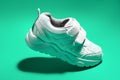 one macro flying white teen sneaker with velcro fasteners isolated on a green background in a minimalist style