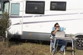 One man digital nomad lifestyle working on alternative outside workplace desk with a camper van motorhome house in background. Royalty Free Stock Photo