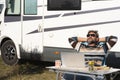 One man digital nomad lifestyle working on alternative outside workplace desk with a camper van motorhome house in background. Royalty Free Stock Photo