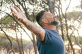 One man outstretching arms in front of a high trees forest and sunset sunlight. Concept of environment and healthy lifestyle. Royalty Free Stock Photo