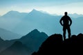 One Man reaching summit after climbing and hiking enjoying freedom and looking towards mountains silhouettes panorama Royalty Free Stock Photo