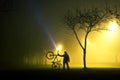 One man is standing and holding the bicycle in foggy and mysterious park.