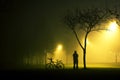 One man is standing and holding the bicycle in foggy and mysterious park.