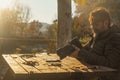 One man using a dslr big camera in outdoor sitting on a wooden table in autumn season. Yellow leaves in a park. Photographer Royalty Free Stock Photo