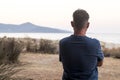 One man viewed from back in landscape contemplation. Tourist looking scenic place destination with ocean and island. Travel people