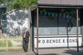 One man well dressed wearing a face mask to protect against covid-19 stands leaning against yellow picket fence in sun beside old