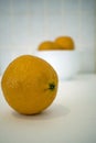 Orange on White with White bowl with oranges in background.