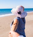 One mature woman walking in the sand of the beach with her husband holding her hand - vacations and holiday outdoors with tourists Royalty Free Stock Photo