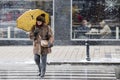 One mature women in furs crossing the street while walking under umbrella on snowy winter day in the city
