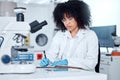 One mixed race scientist with curly hair wearing safety equipment writing notes and analysing medical test samples with