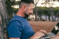 One modern adult man using and working on laptop at the park. Concept of smart working and freelance digital nomad small business Royalty Free Stock Photo