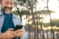 One modern mature man using smartphone outdoor at the park smiling and having fun. Social media life sharing uploading contents. Royalty Free Stock Photo