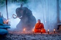 One monk sit and stay in meditate position in front of elephant lie down on background at night in concept of lifestyle relate